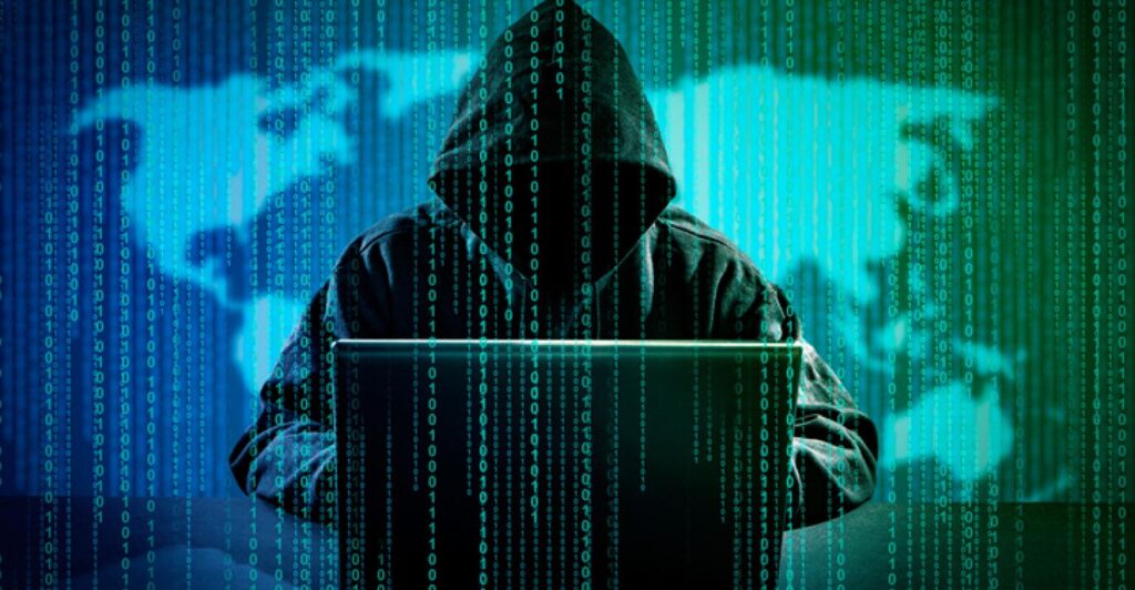 Man in hoodie typing on his laptop with binary code running down the screen. By Scyther5 on iStock.